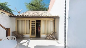 Un petit pati amb teulada de rajola, dues cadires de fusta, una taula blanca i una porta que dona a l'interior.