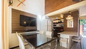 Cuina moderna amb televisió de pantalla plana, nevera i microones. Hi ha una zona de menjador amb taula de vidre i cadires blanques.