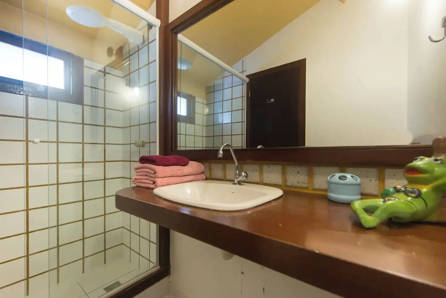 Un baño con lavamanos, espejo y un juguete de rana verde sobre el mostrador.