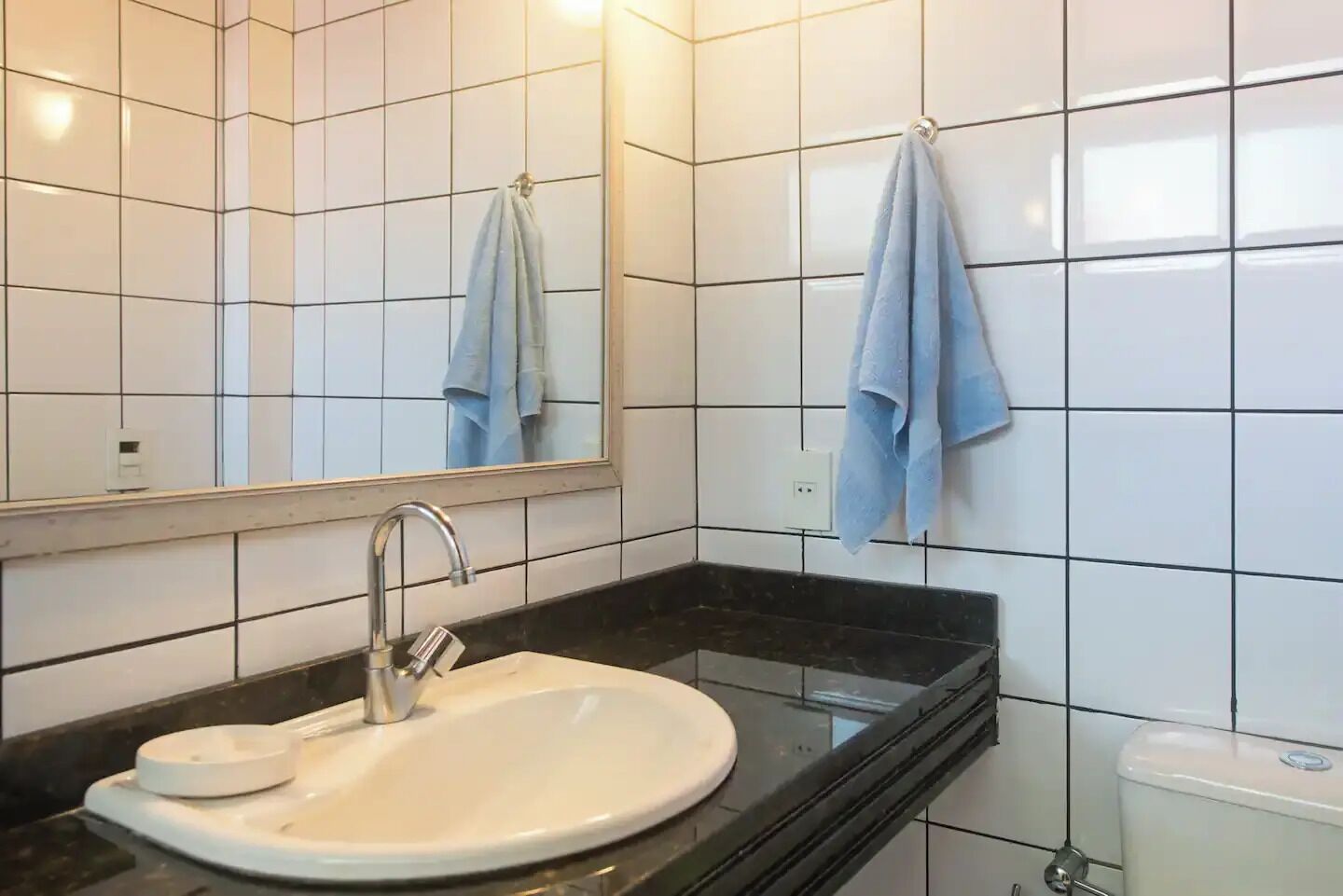 Een badkamer met een witte wasbak, een zwart aanrecht en een spiegel erboven. Twee handdoeken hangen aan de muur.