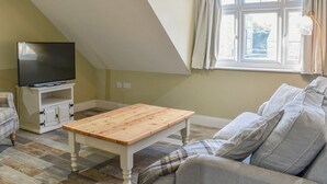 A living room with a television on a white cabinet, a wooden coffee table, a sofa, and a window with curtains.