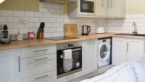 A compact kitchen with white cabinets, a microwave, a kettle, and a dishwasher.