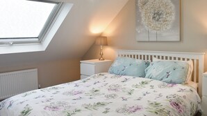 A bedroom with a skylight, a bedside lamp, a floral bedspread, and a wall-mounted artwork.