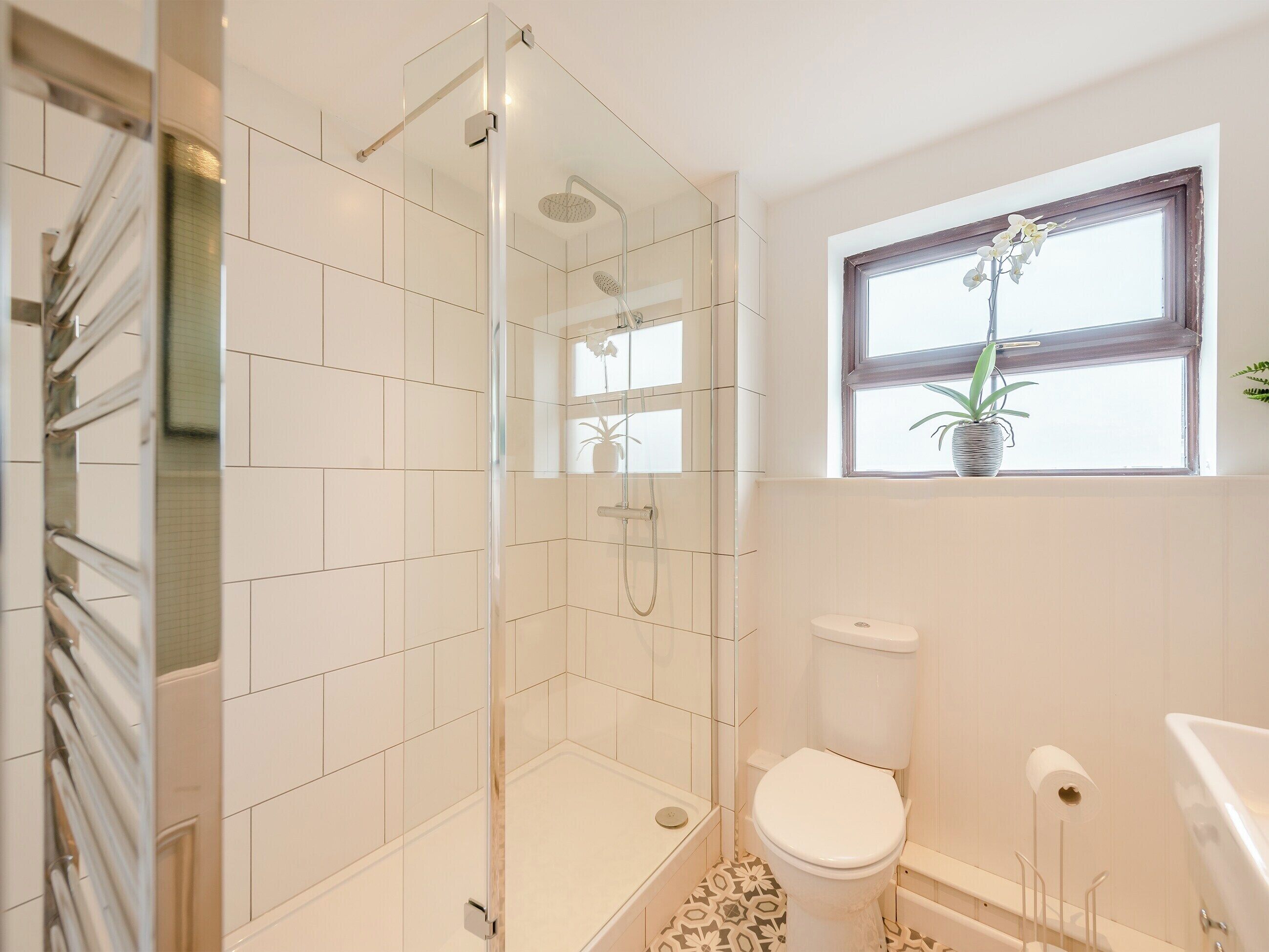 Ein modernes Badezimmer mit einer Duschkabine aus Glas, einer Toilette und einem Fenster mit einem Blumentopf.