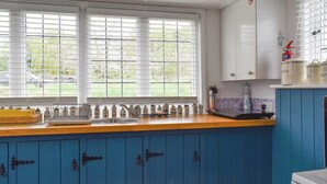 A kitchen with blue cabinets, a wooden countertop, and a window with blinds.