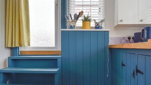 A kitchen with blue cabinets, a window with blinds, a sink, and a countertop with a plant and utensils.