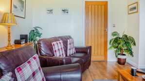Un salon avec un canapé en cuir marron, une porte en bois et une plante en pot.