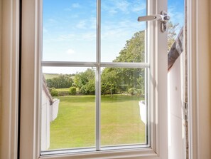 A view through a window with a white frame, revealing a well-maintained lawn and trees in the background.