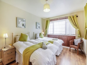 A bedroom with two beds, a bedside table, a lamp, a chair, and a window with curtains.
