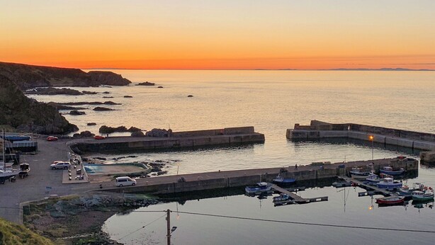 Een kustjachthaven met boten aanmeren, een weg die naar het water leidt, en een zonsondergang op de achtergrond.
