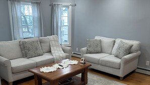 Una sala de estar con dos sofás de color gris claro, una mesa de centro de madera y una alfombra gris.