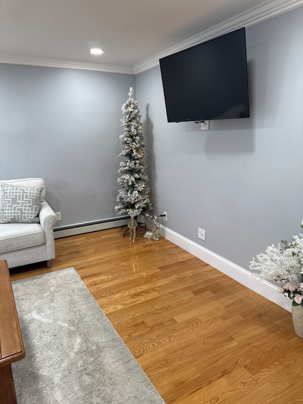 A living room with a grey wall, a flat-screen TV mounted above a fireplace, a white sofa, and a small Christmas tree. - Family Friendly (Manchester)