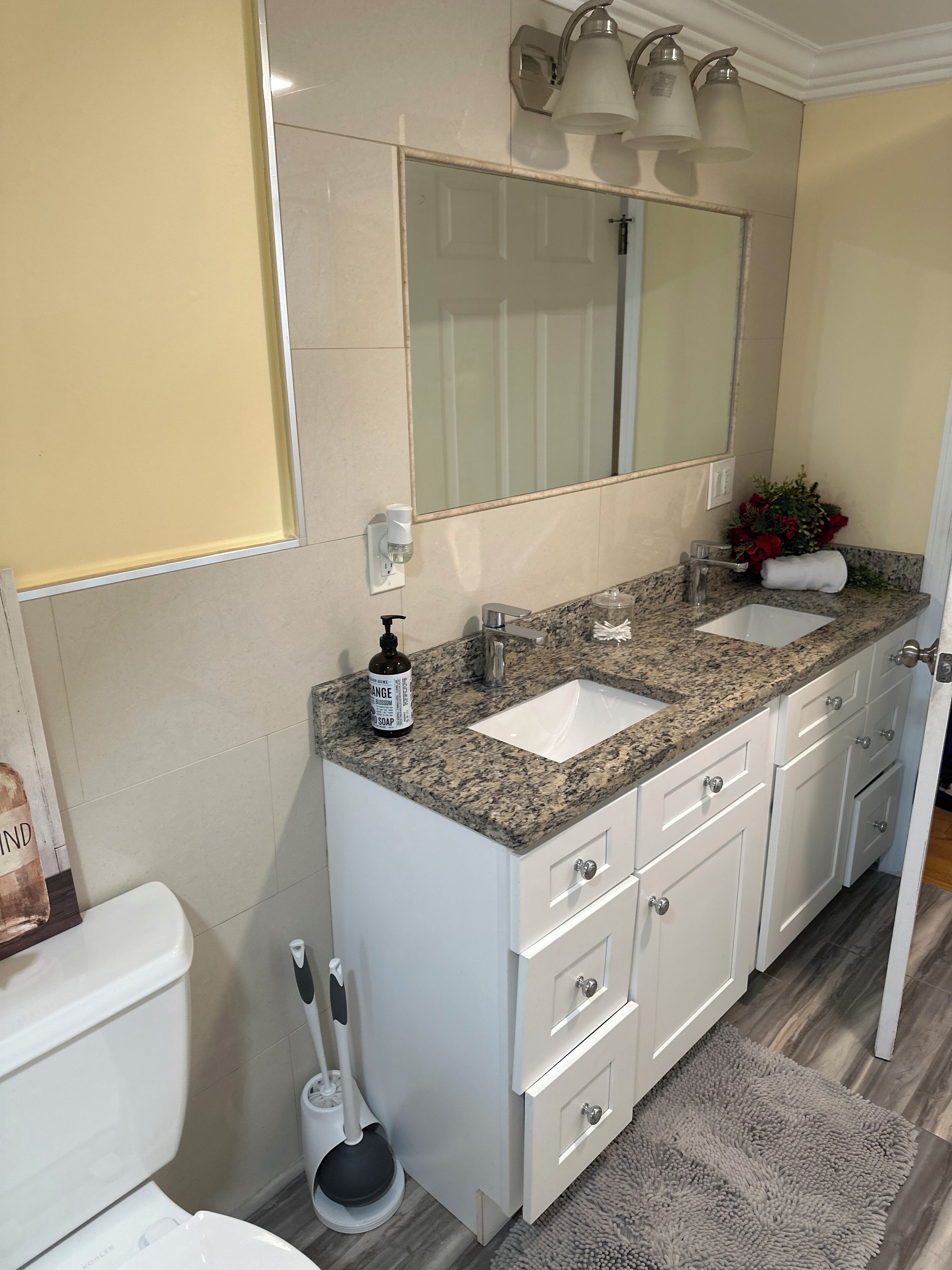 Une salle de bain moderne avec un lavabo surmonté d’un plan de travail en granit, un grand miroir et des meubles blancs.