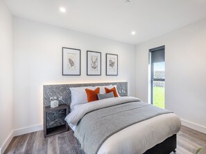 A modern bedroom with a bed, nightstand, and framed botanical prints on the wall. - Cybi Lodge 6 - UK42798 (Llangefni)