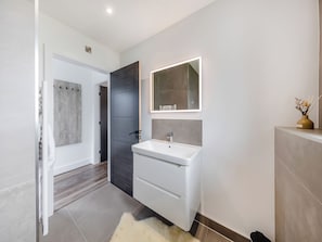 A modern bathroom with a white sink, a dark door, and a mirror above it.