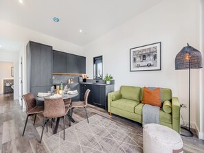 A modern living space with a dining area, kitchen, and a green sofa with cushions. - Cybi Lodge 6 - UK42798 (Llangefni)