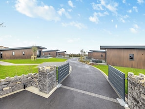A modern building complex with a paved entrance, stone walls, and a clear sky.