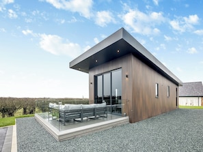 A modern building with a sloped roof, large glass doors, and a deck with benches.