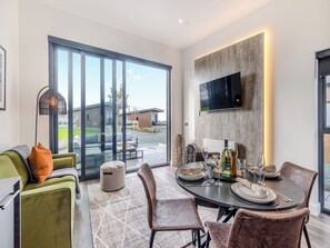 A modern dining area with a large table, chairs, and a flat-screen TV mounted on the wall. - Cybi Lodge 6 - UK42798 (Llangefni)