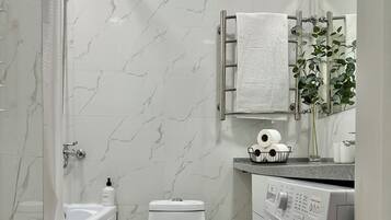 Een moderne badkamer met een douche, toilet en wasmachine.
