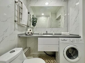 Un baño moderno con salpicadero de mármol, un lavabo con espejo superior, inodoro y lavadora de carga frontal.