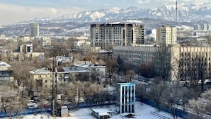 A cityscape with buildings, a snow-covered mountain range, and a tower in the distance.