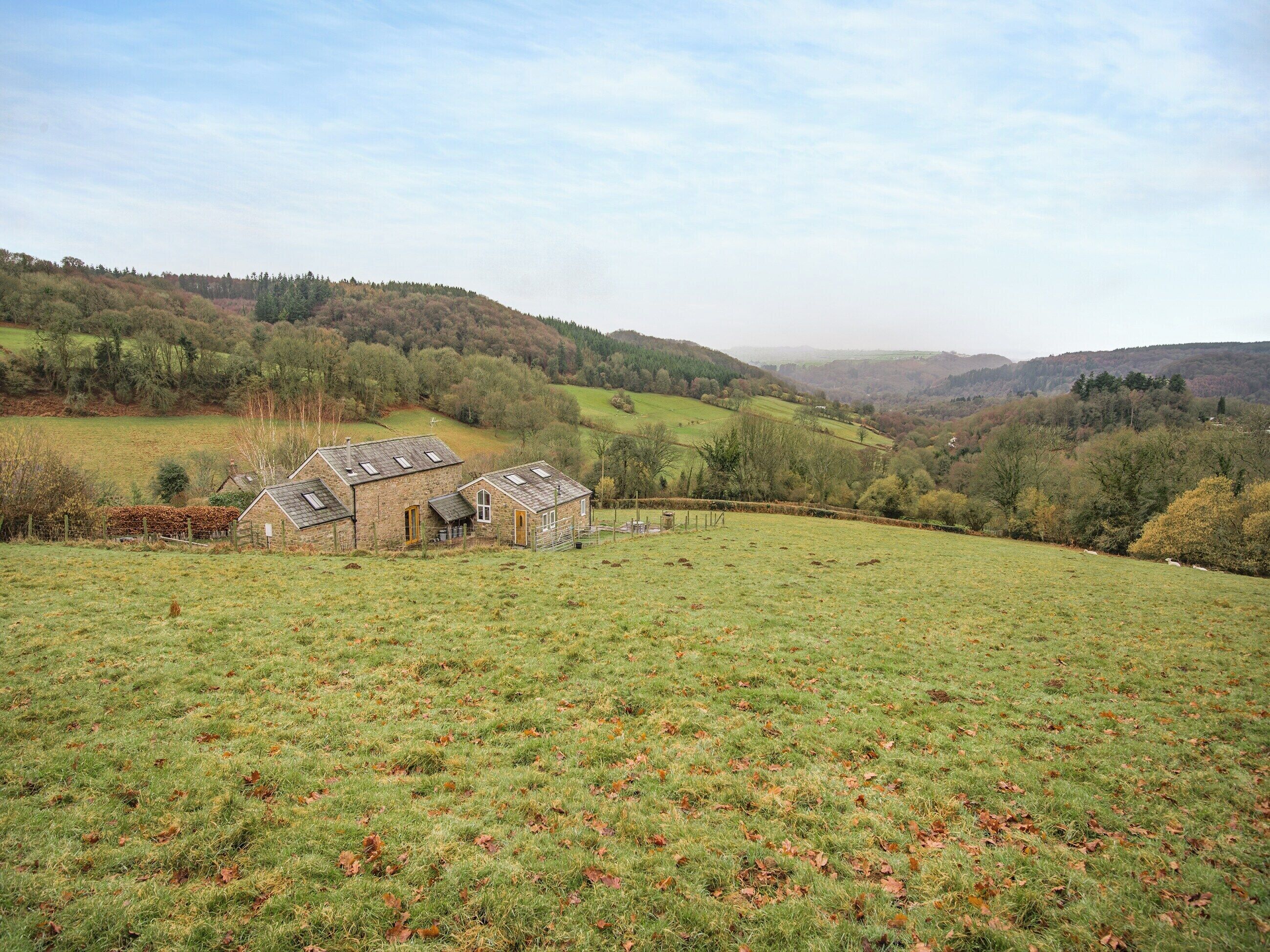 A rural landscape with a stone barn and a grassy field.