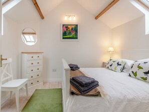 Un dormitorio con cama, cómoda, silla, alfombra verde, un cuadro y una lámpara.