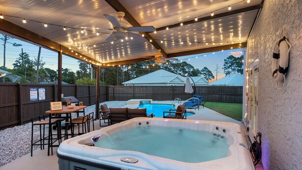 A covered outdoor area with a hot tub, seating, and string lights. - PCB Paradise Sands Oasis - Private Pool, Game Room, Hot Tub! (Panama City Beach)