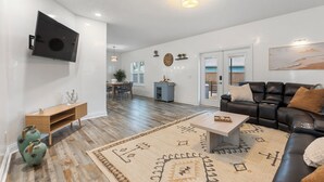 A spacious living room with a flat-screen TV mounted on the wall, a black leather sofa, a coffee table, and a patterned rug. - PCB Paradise Sands Oasis - Private Pool, Game Room, Hot Tub! (Panama City Beach)