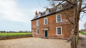 Une maison à deux étages, construite en briques, avec une allée en gravier et une clôture en bois.