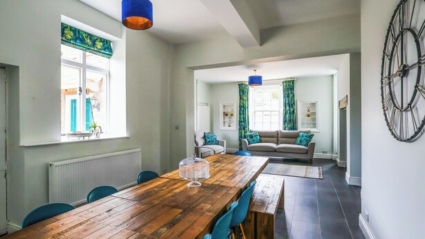 Un coin repas avec une table en bois, des chaises bleues et un ventilateur de plafond.