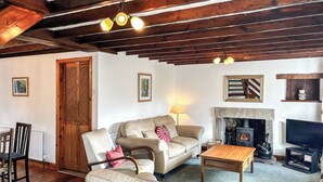 Uma sala de estar acolhedora com lareira, vigas de madeira no teto, sofá, mesa de centro e televisão.
