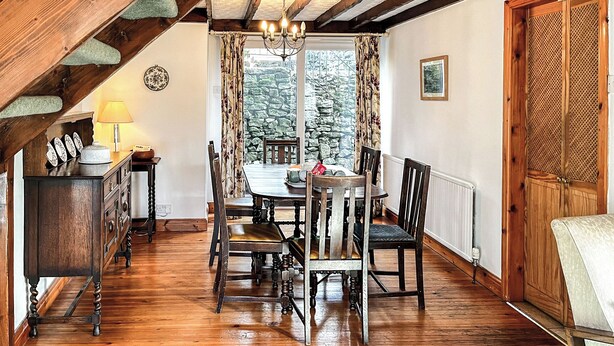 Uma sala de jantar com uma mesa e cadeiras de madeira, um candelabro e vista para árvores através de uma janela.