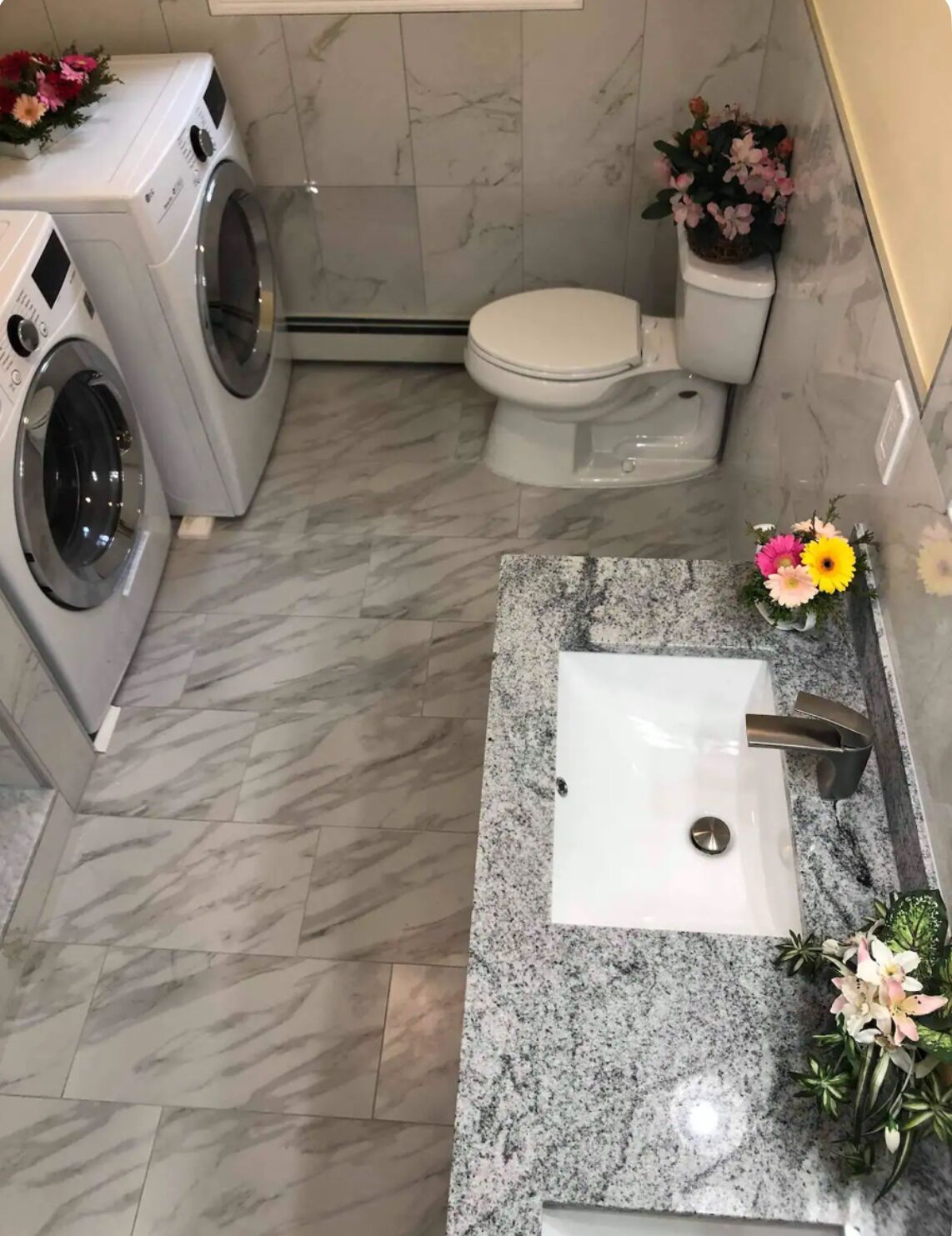 A bathroom with a marble floor, a sink with a modern faucet, a toilet, and a washing machine.