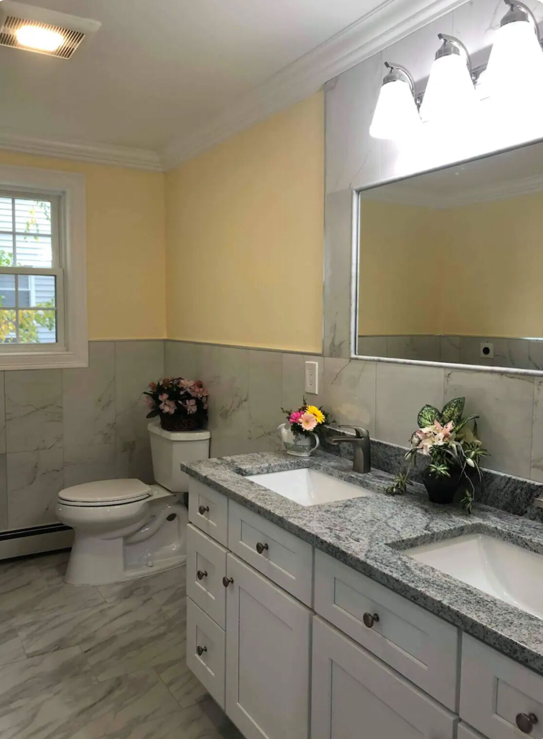 Une salle de bain avec des toilettes blanches, un lavabo doté d’un plan de travail en marbre et un miroir au-dessus du lavabo.