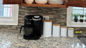 Ett kök med träskåp, en kaffemaskin från Keurig och en bänkskiva i granit.
