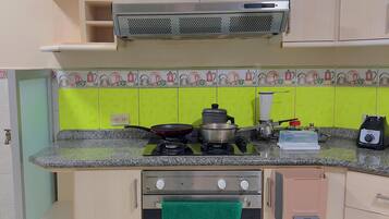 Une cuisine compacte équipée d’une cuisinière, d’un four et d’un four à micro-ondes. On y trouve des placards au-dessus du plan de travail et une hotte aspirante au-dessus de la cuisinière.