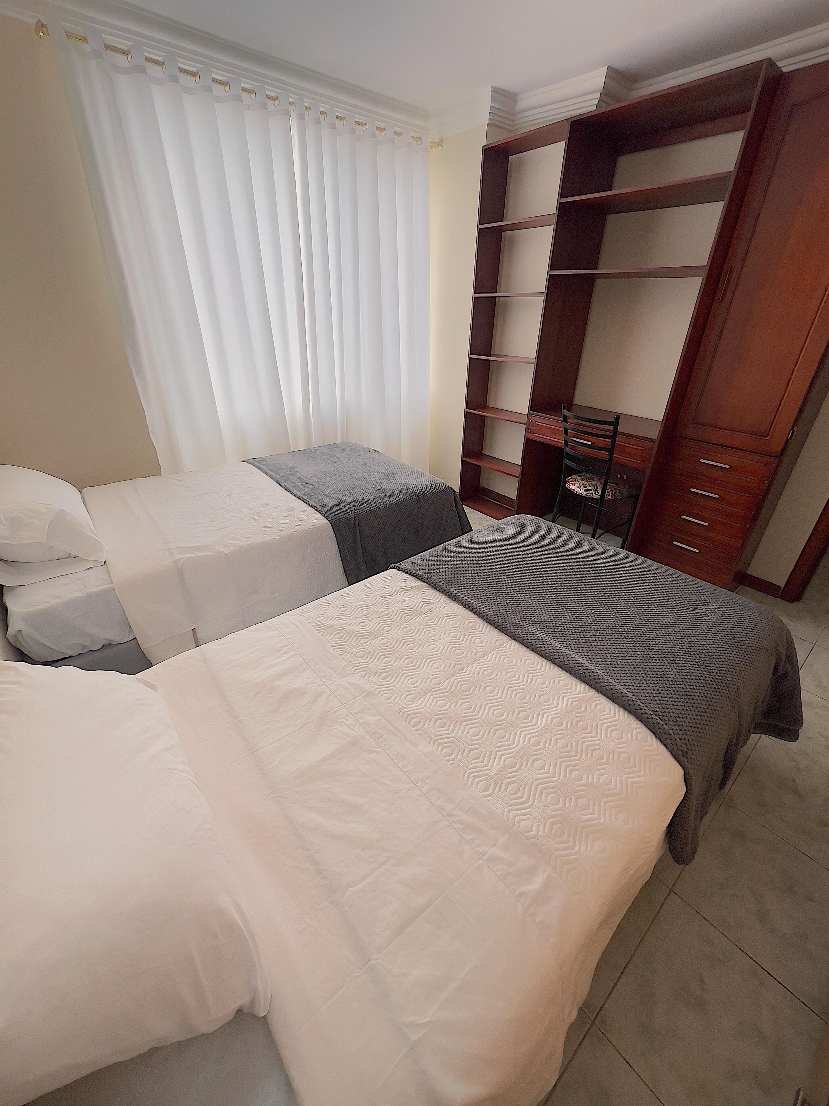 A hotel room with two beds, a wooden wardrobe, and a chair.