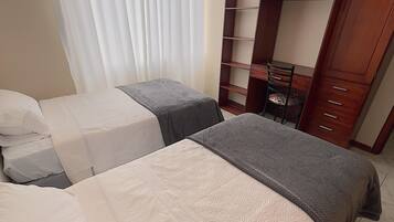 A hotel room with two beds, a wooden wardrobe, and a chair.