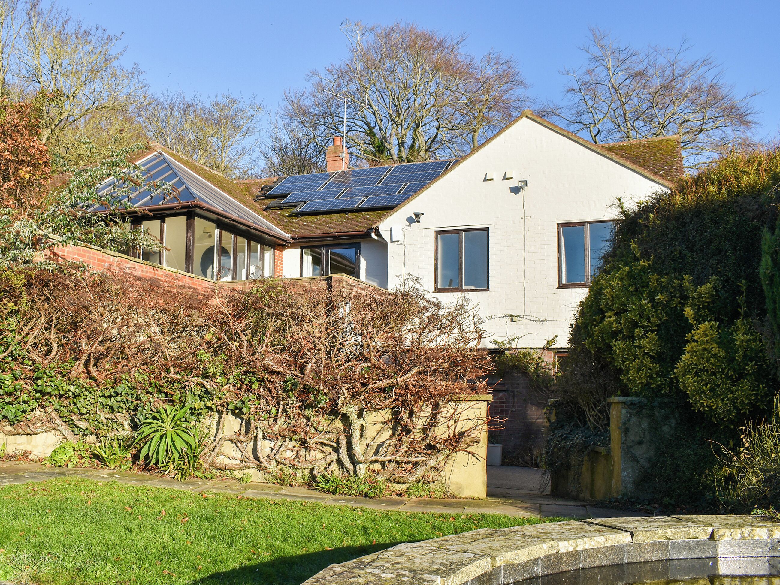 Une maison avec des panneaux solaires sur le toit, un jardin avec un bassin et un mur en briques.