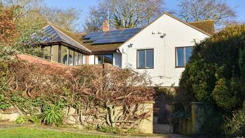 A house with solar panels on the roof, a garden with a pond, and a brick wall.