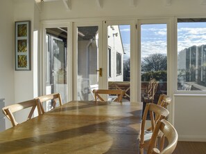 A dining area with a wooden table and chairs, large windows, and a view of a building outside. - Pines Cottage - UK42110 (St. Margaret&rsquo;s Bay)