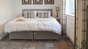 A neatly made bed with a grey headboard, a bedside table with a lamp, and three framed pictures on the wall. - Pines Cottage - UK42110 (St. Margaret&rsquo;s Bay)