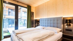 A modern bedroom with a large bed, two bedside lamps, and a view of a building through a glass door. - Appealing Apartment With Pool (Sankt Georgen am Kreischberg)