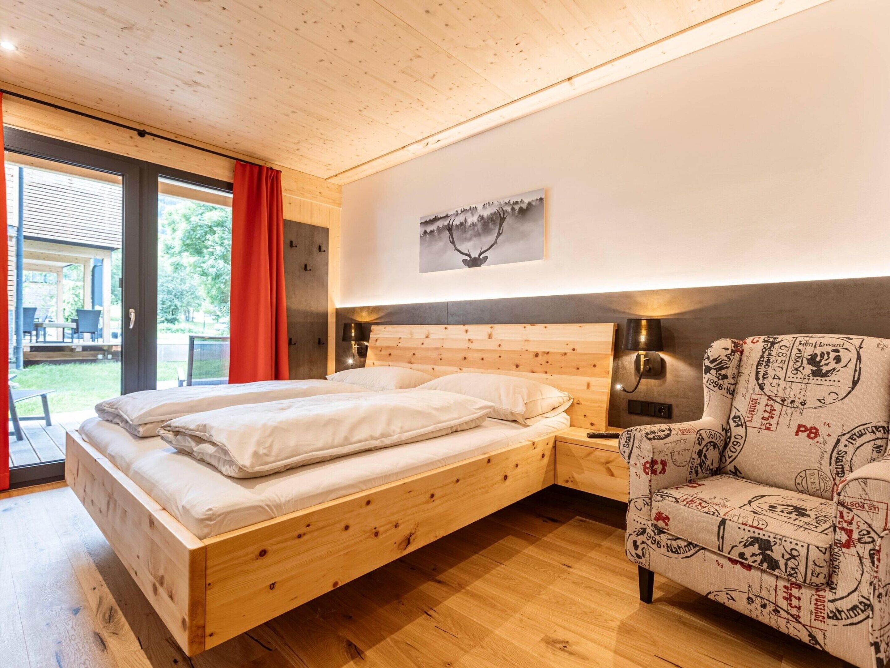 Ein Schlafzimmer mit einem hölzernen Bett, einem Stuhl mit Vintage-Muster und einem Bild an der Wand.