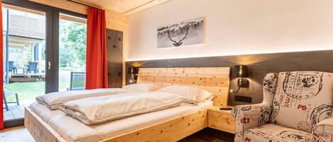 A bedroom with a wooden bed, a chair with a vintage pattern, and a painting on the wall.