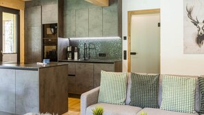 A modern kitchen with a central island, built-in cabinets, and a backsplash. There is a sofa with patterned cushions and a small plant on the floor. - Appealing Apartment With Pool (Sankt Georgen am Kreischberg)