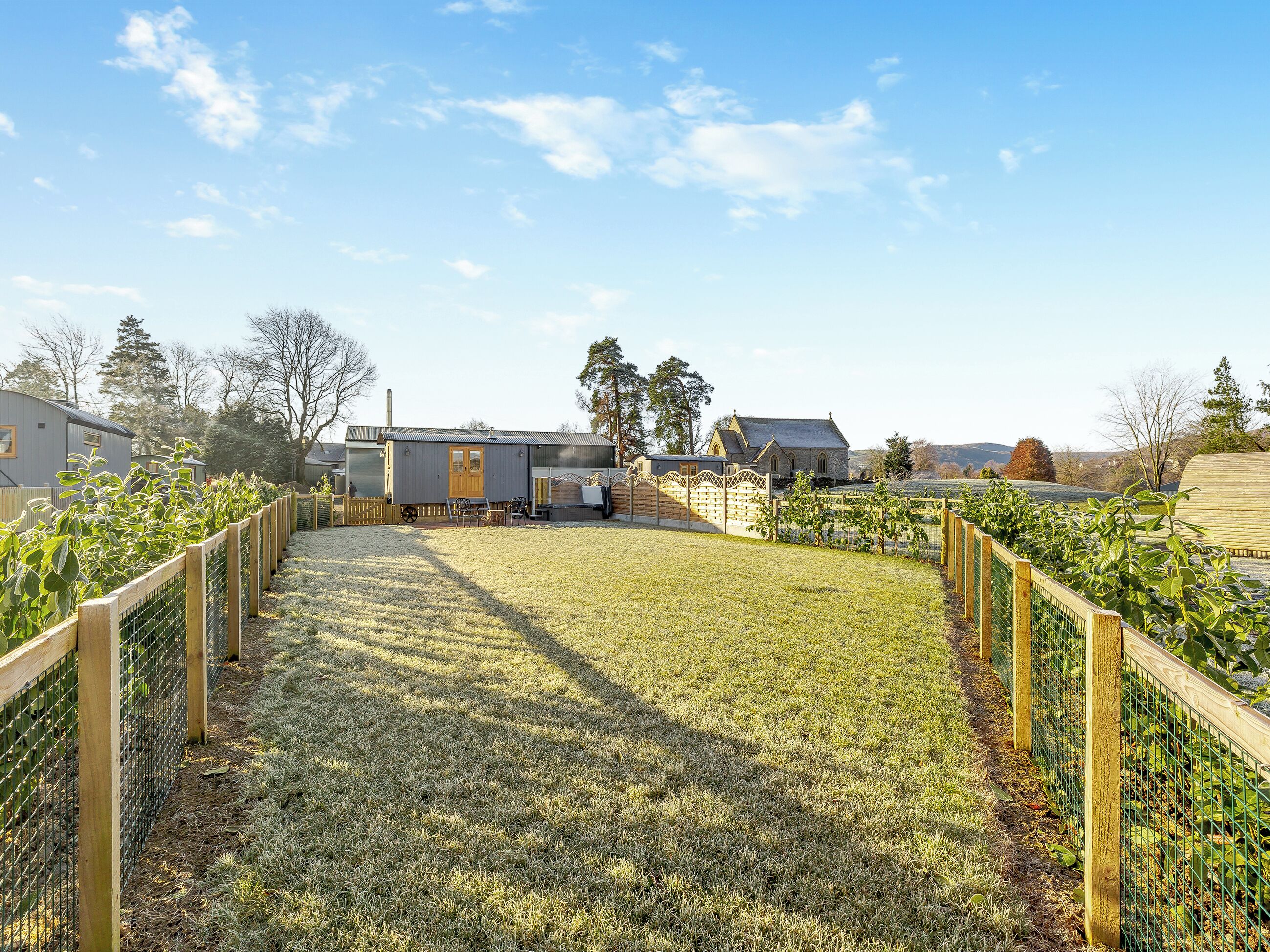 A rural property with a fenced pathway leading to a house with a gabled roof and a chimney.