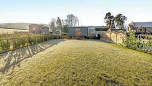 Een landelijk pand met een omheinde tuin, een kleine schuur en een stenen gebouw met een puntdak.
